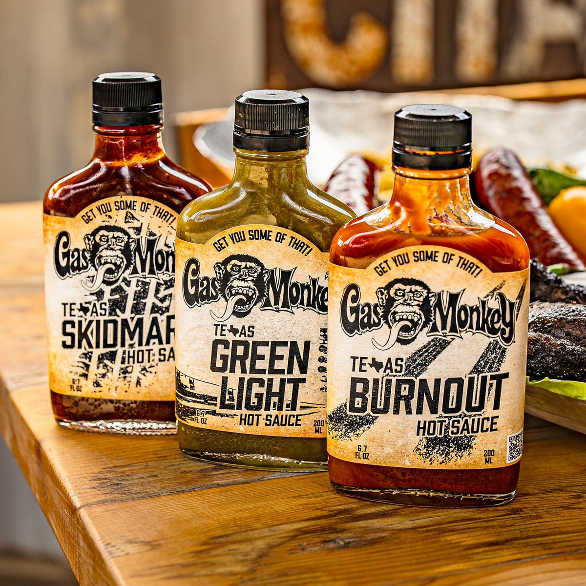 Front view of GMG Hot Sauce Variety Pack showing Texas Skidmark, Green Light, and Burnout bottles on a wooden table