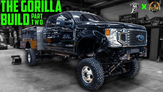 Front three-quarter view of a black utility truck showcasing lifted suspension in a garage, with The Gorilla Build Part Two