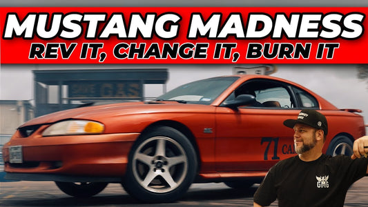 Orange Mustang driving past a man in a black shirt and cap on a paved surface