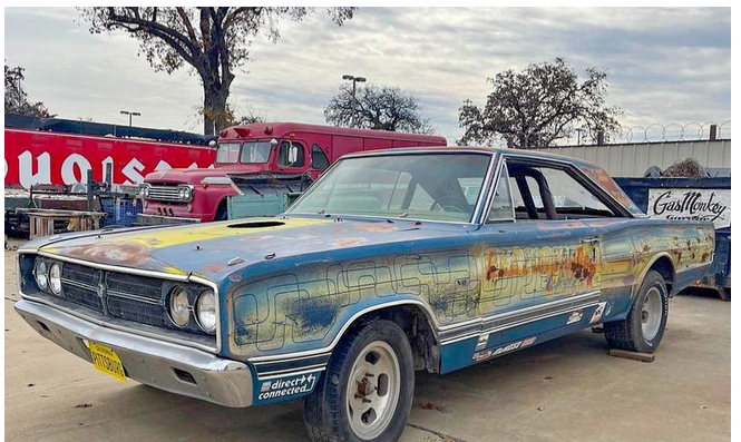 Front three-quarter view of a 1967 Dodge Coronet showcasing its weathered blue finish with an outdoor garage backdrop