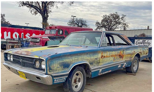 Front three-quarter view of a 1967 Dodge Coronet showcasing its weathered blue finish with an outdoor garage backdrop