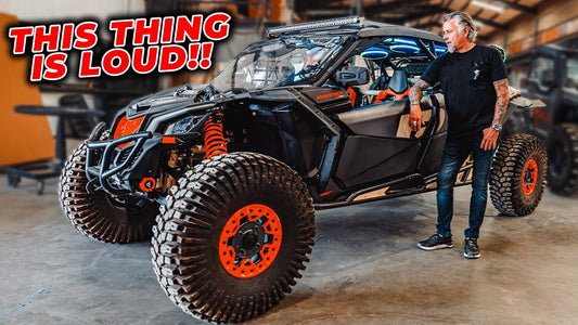 Man stands beside a Cam-Am Maverick side-by-side in a garage under the headline “This Thing Is Loud!!”
