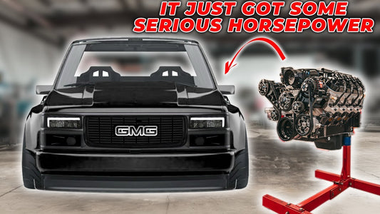 Front view of a black GMC truck beside an engine on a stand, with headline text ‘It just got some serious horsepower’