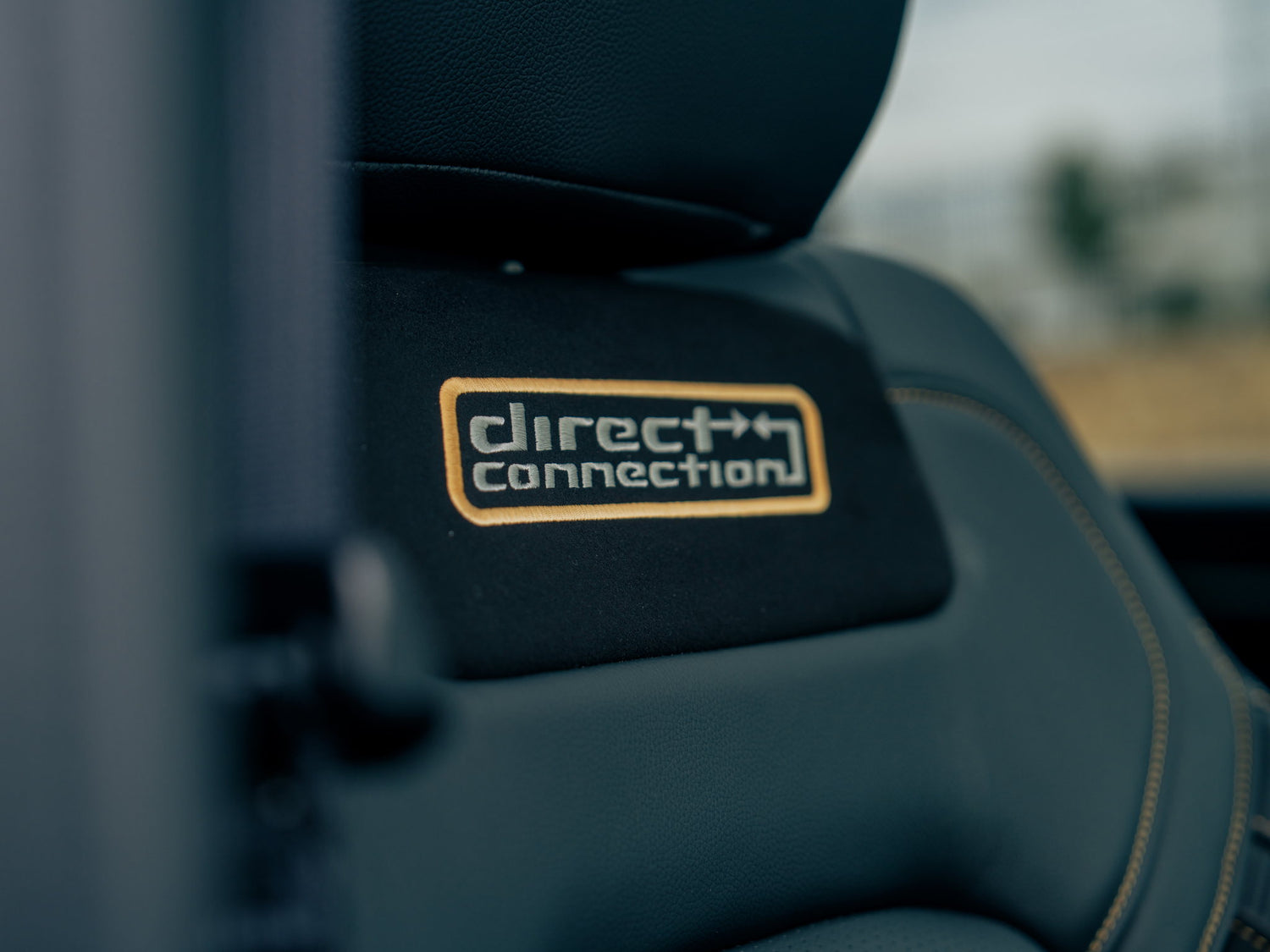 Close-up of Fox Factory Ram seat showcasing Direct Connection badge and gold stitching in a dark interior