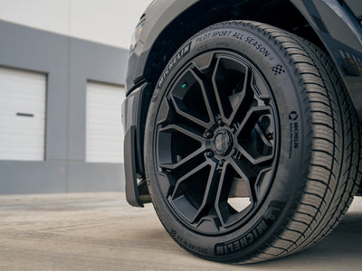 Close-up of the Fox Factory Ram showcasing a black 22-inch wheel and performance tire outside a warehouse