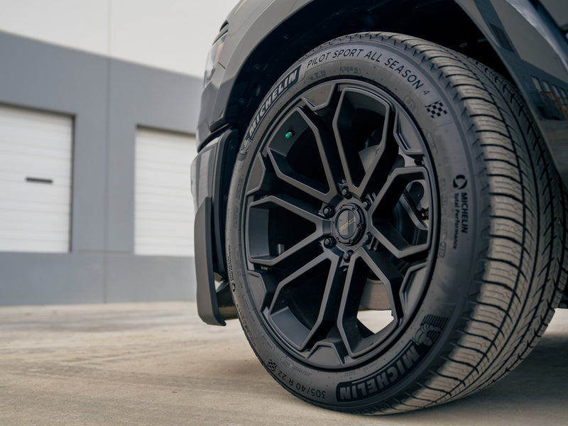 Close-up of the Fox Factory Ram showcasing a black 22-inch wheel and performance tire outside a warehouse